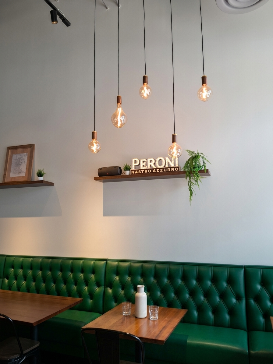 Cozy café booth with green tufted seating, wooden tables, hanging lights, and a shelf sign reading “PERON.”