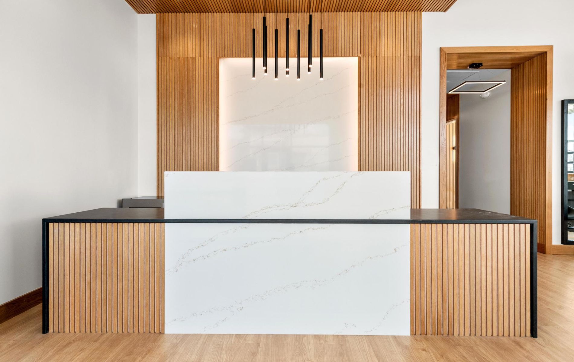 Modern reception desk with wood slats, white marble panels, and black accents in a bright room