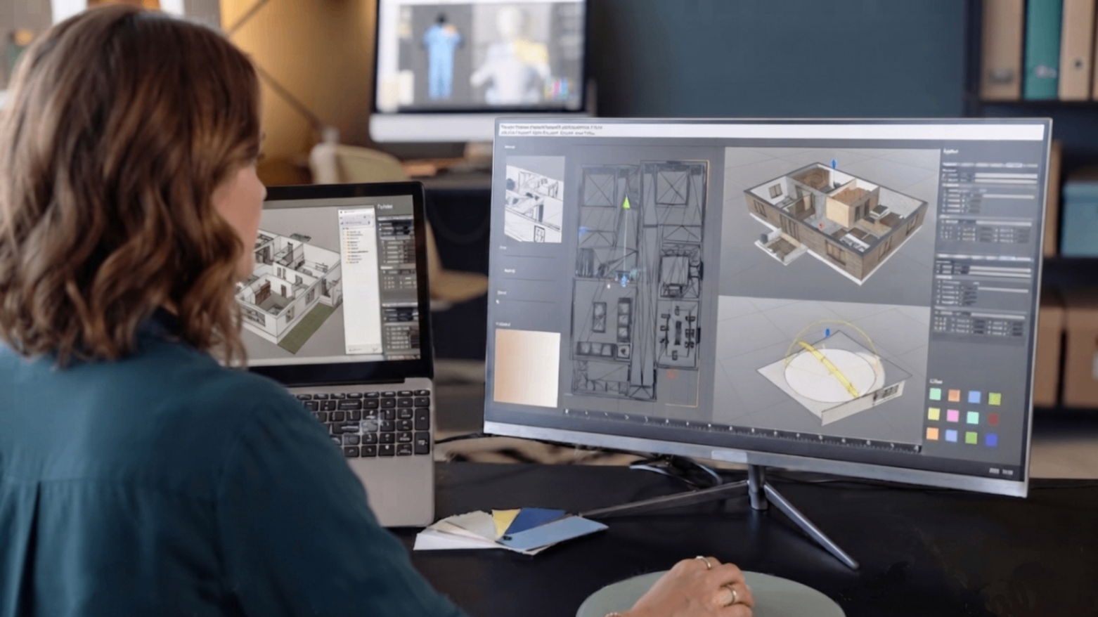 Person working at a desk with dual monitors showing architectural design plans and 3D model visuals