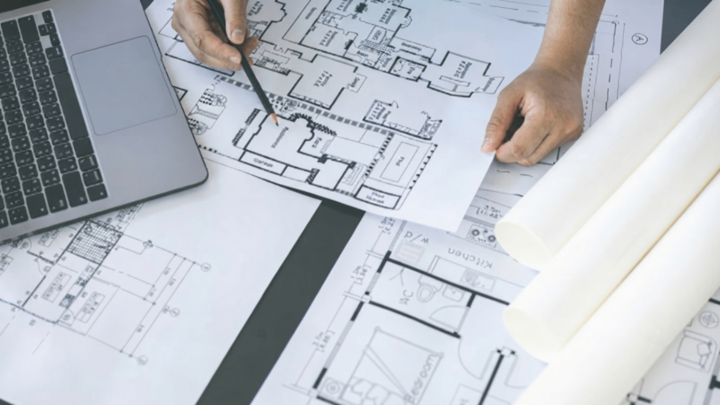 Hands pointing at architectural floor plans beside a laptop on a desk