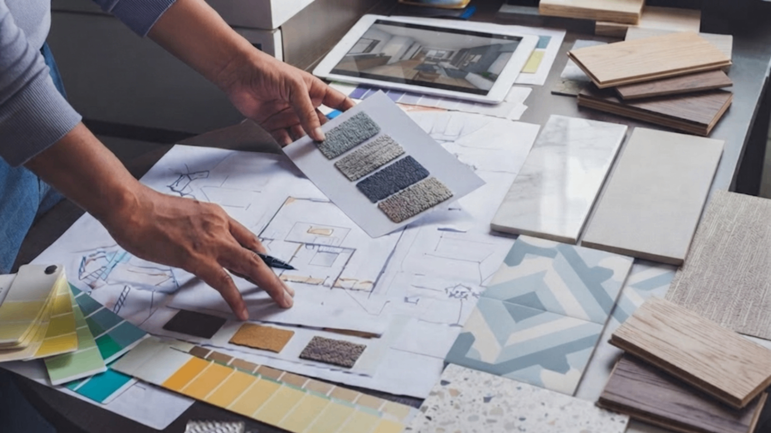 Hands arranging design samples, color swatches, and floor plan prints on a workspace table