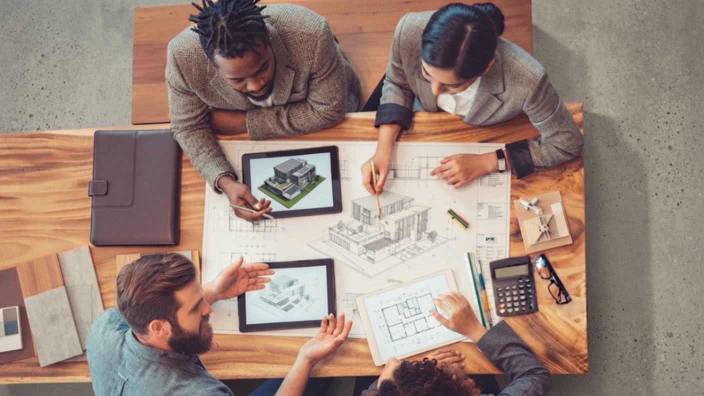 Three people collaborate over floor plans and sketches at a table with a laptop and calculator.