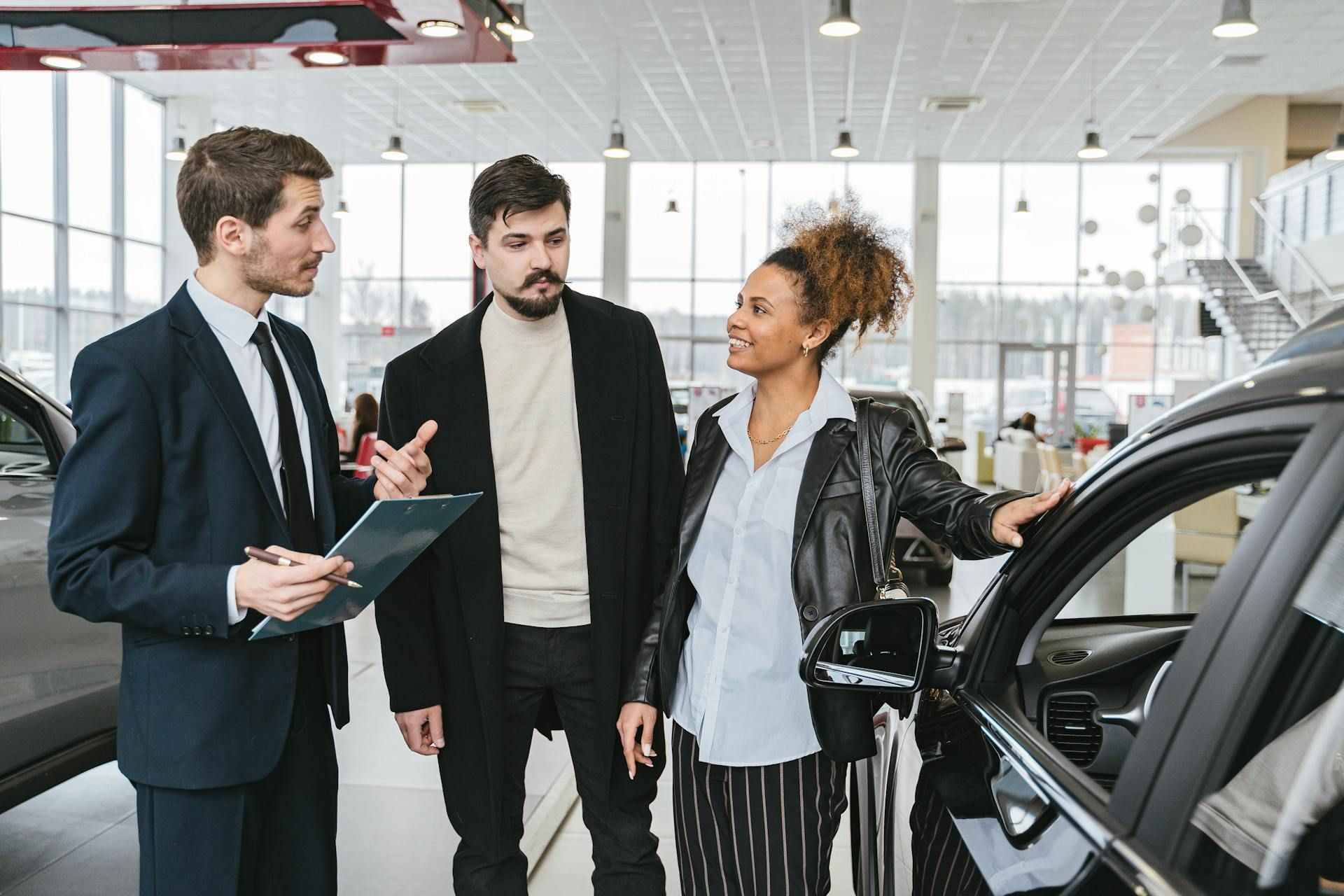 Car salesperson showing a car to two customers in a bright dealership showroom