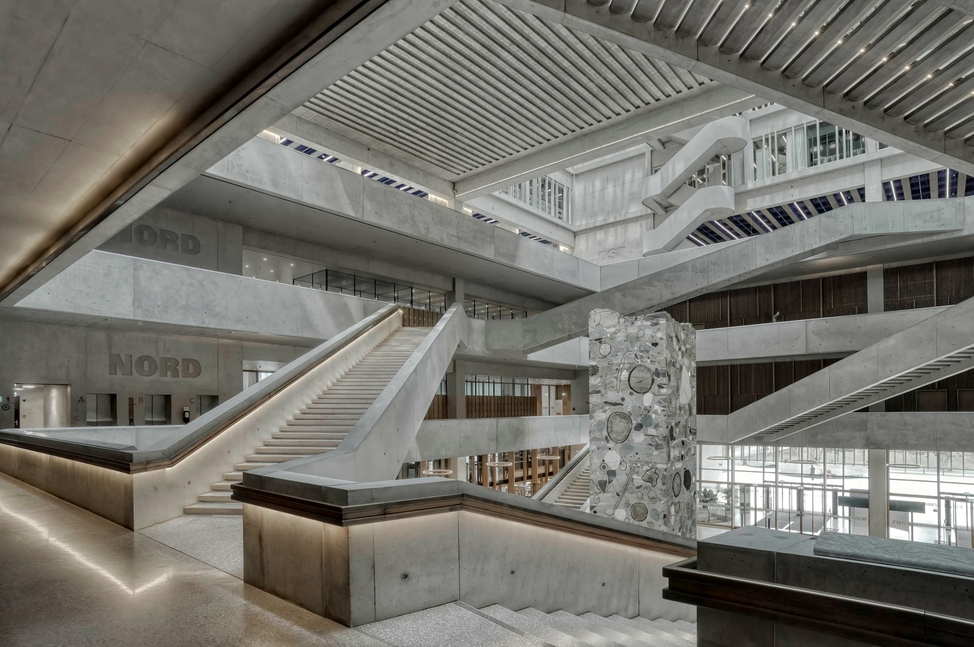Modern atrium interior with wide staircases, skylights, and concrete and glass architecture