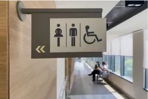 Restroom and wheelchair accessibility sign hanging in a hallway with people seated by windows