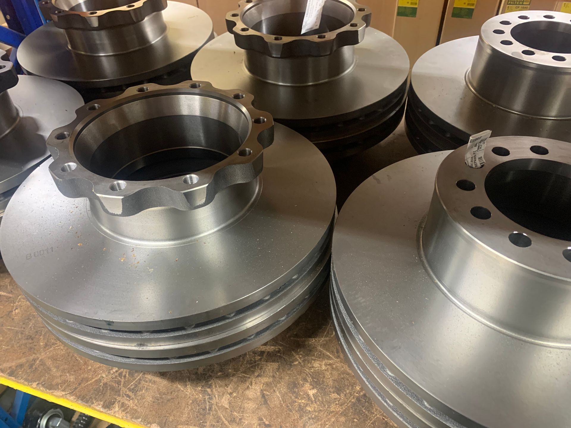 Several shiny, new silver disc brake rotors stacked on a surface.