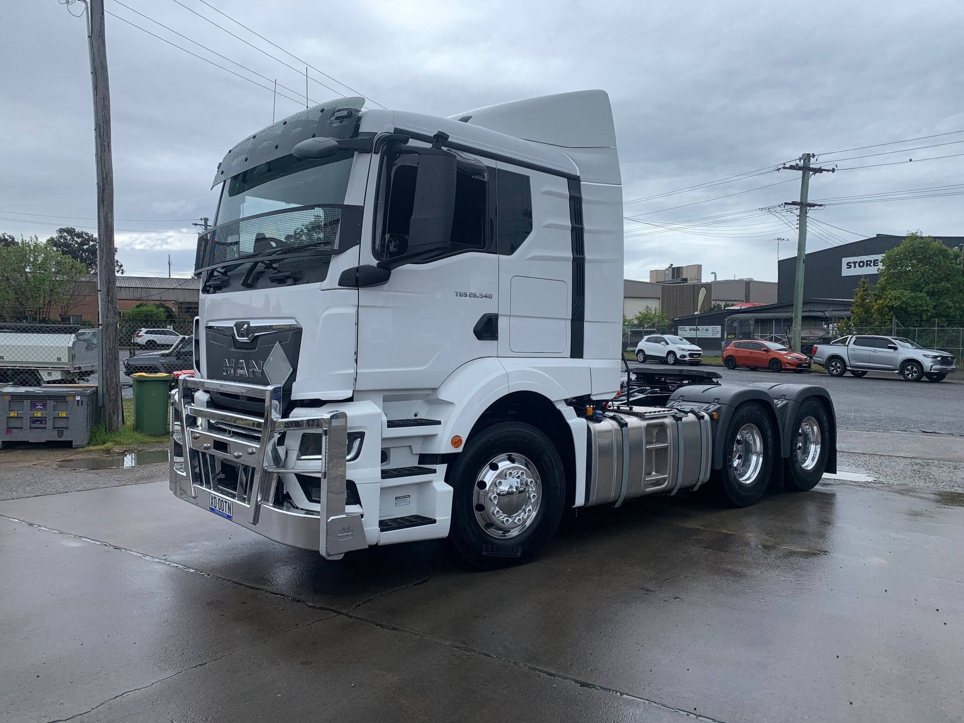White semi-truck parked on wet pavement; a commercial building is in the background.