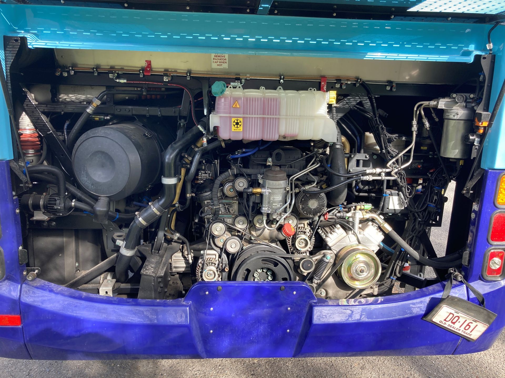Bus engine compartment with engine, coolant tank, and various components. Blue and black colors.