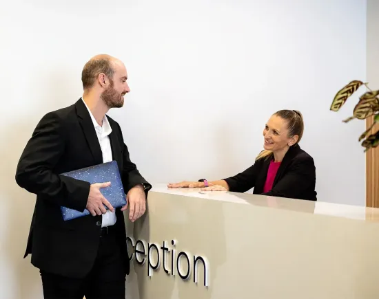 Two people talking at a reception desk in a bright office lobby