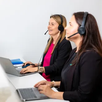 Two headset-wearing customer service agents working at laptops in an office