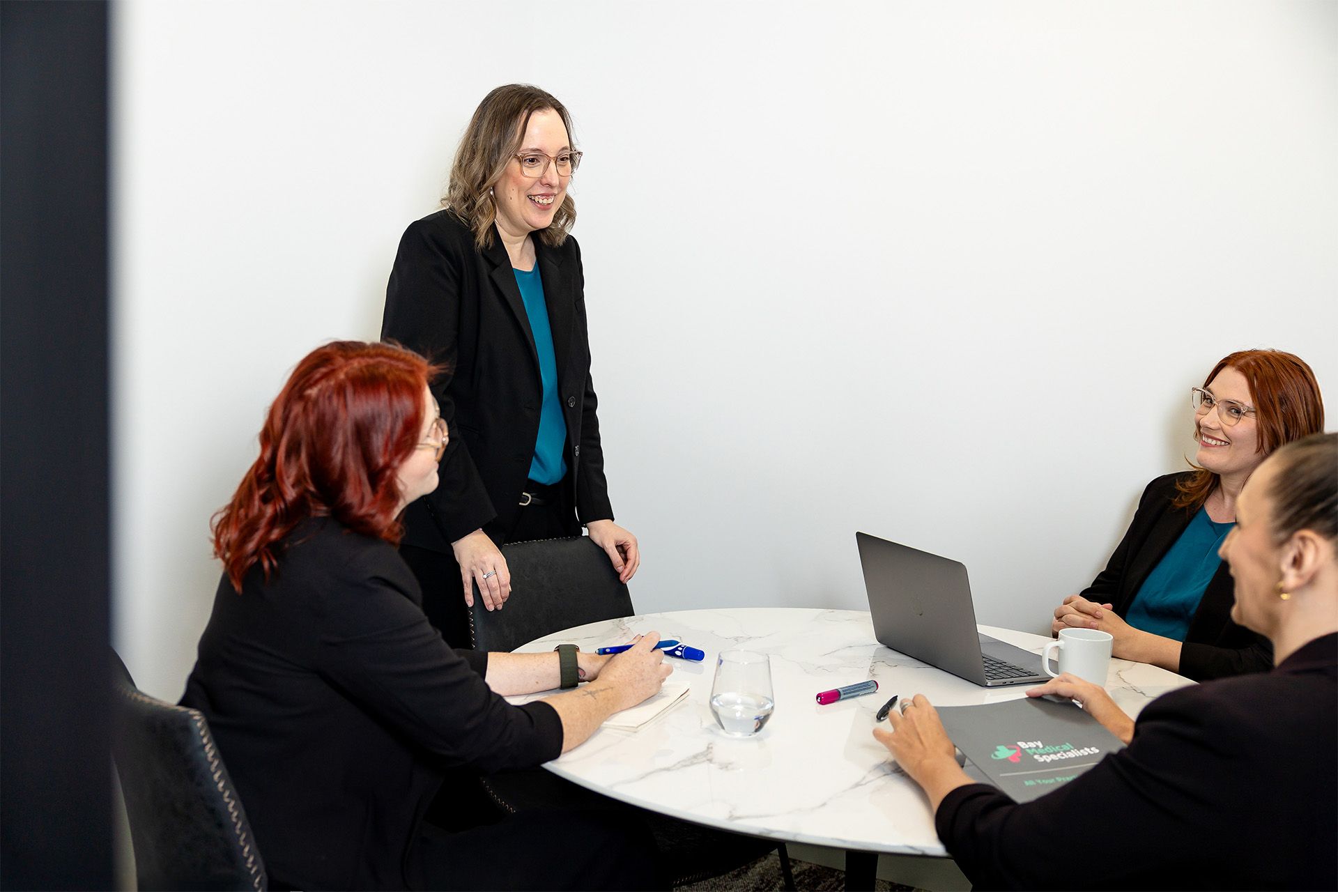 Four coworkers in a meeting around a laptop at a round table in a bright office
