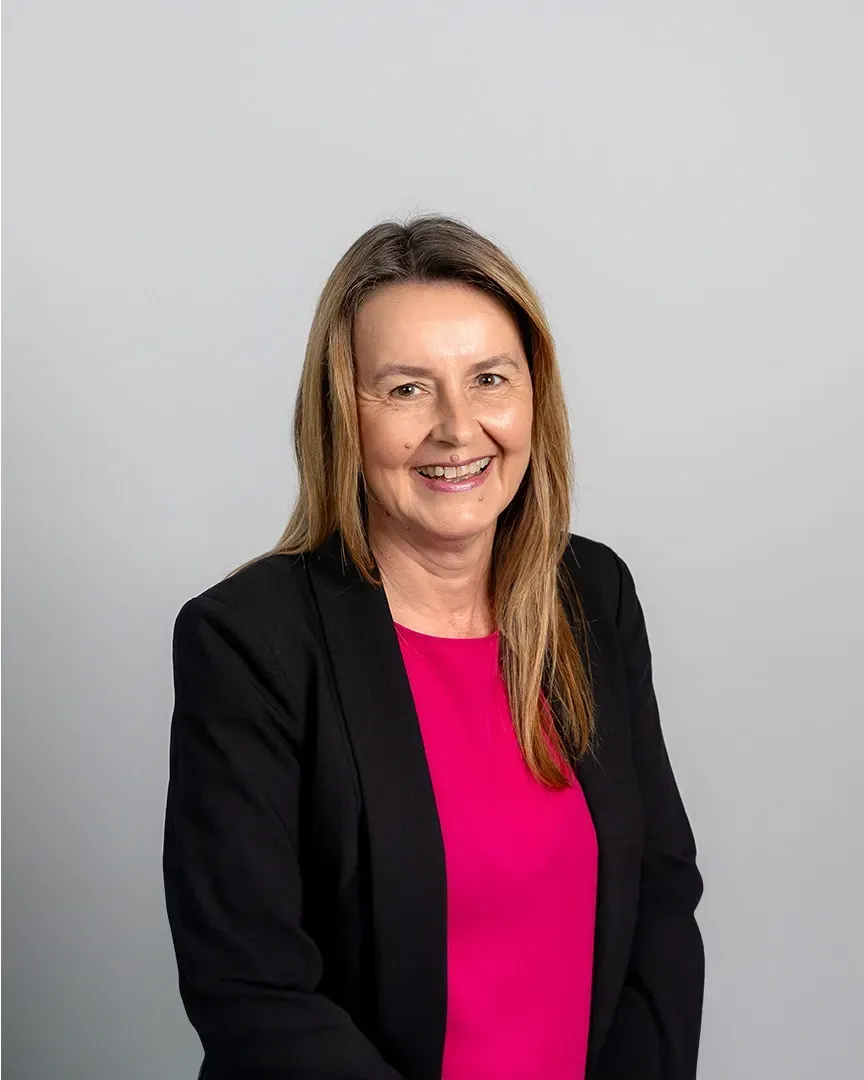 Professional portrait of a smiling woman in a black blazer and bright pink top against a gray background