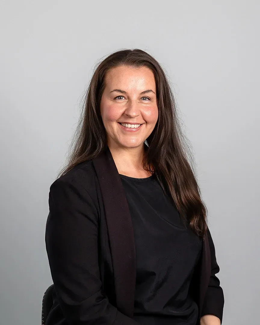 Smiling woman in a black blazer against a light gray background