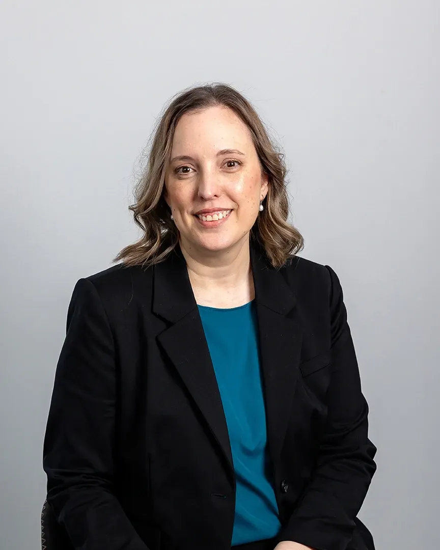 Woman in a black blazer and teal top smiling against a gray background