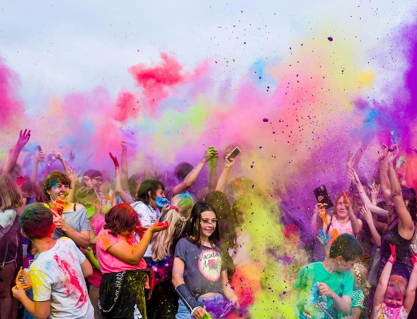 A group of people celebrating at a colorful Holi festival with bright powder clouds filling the air.