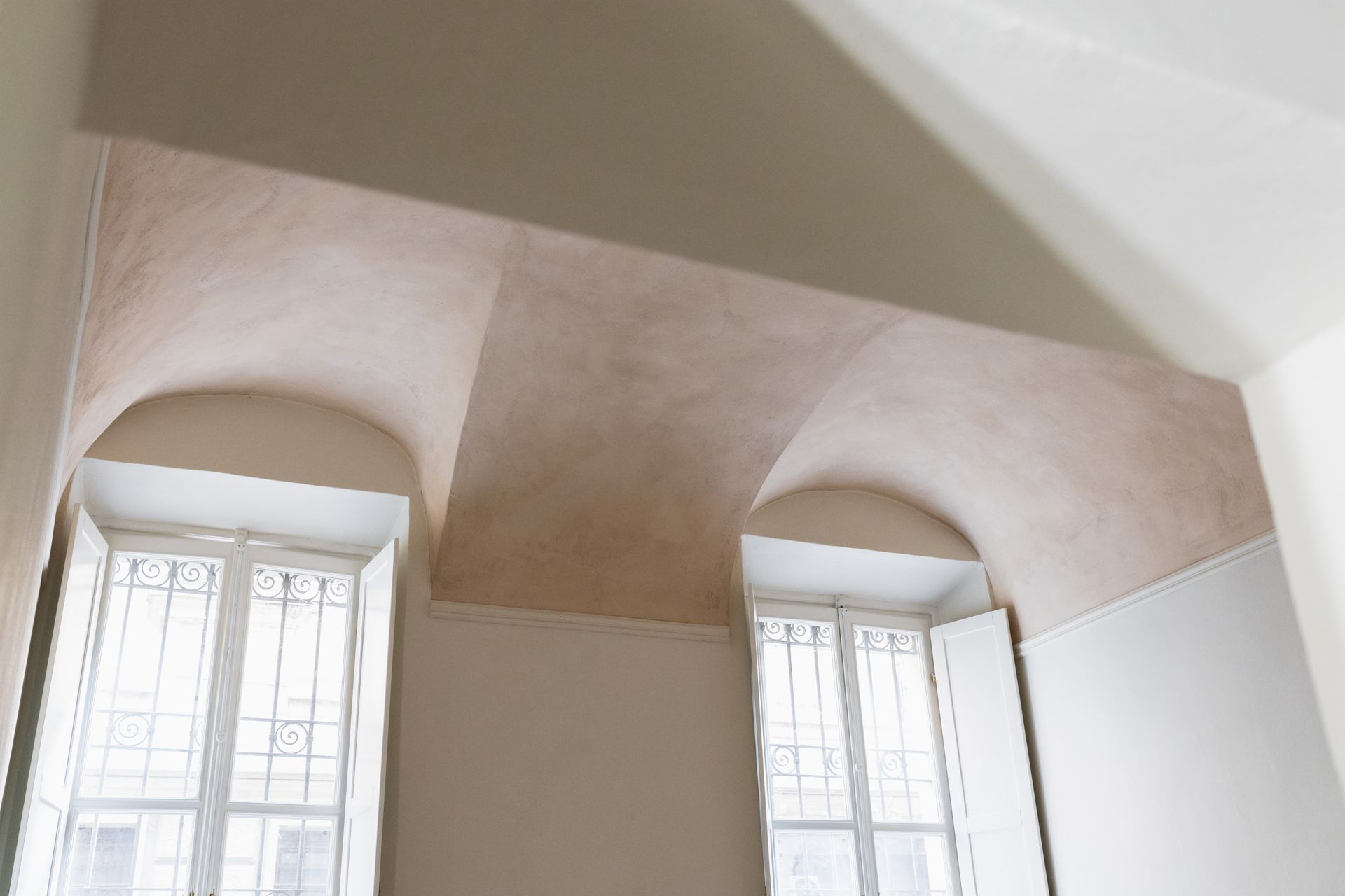 Soffitto a volta sopra alte finestre in una stanza luminosa dalle pareti bianche.