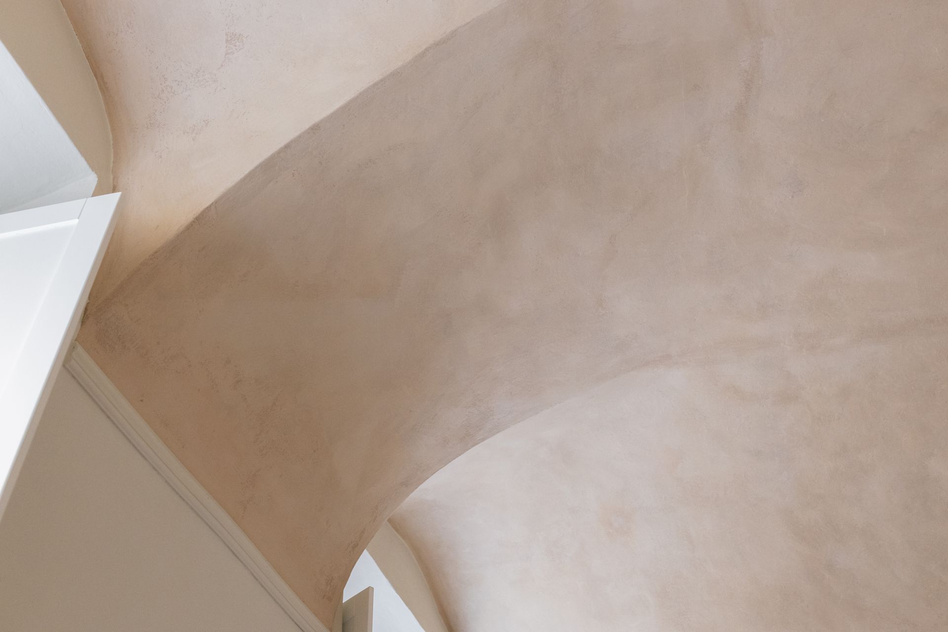 Arco curvo in gesso beige e soffitto con morbida luce naturale
