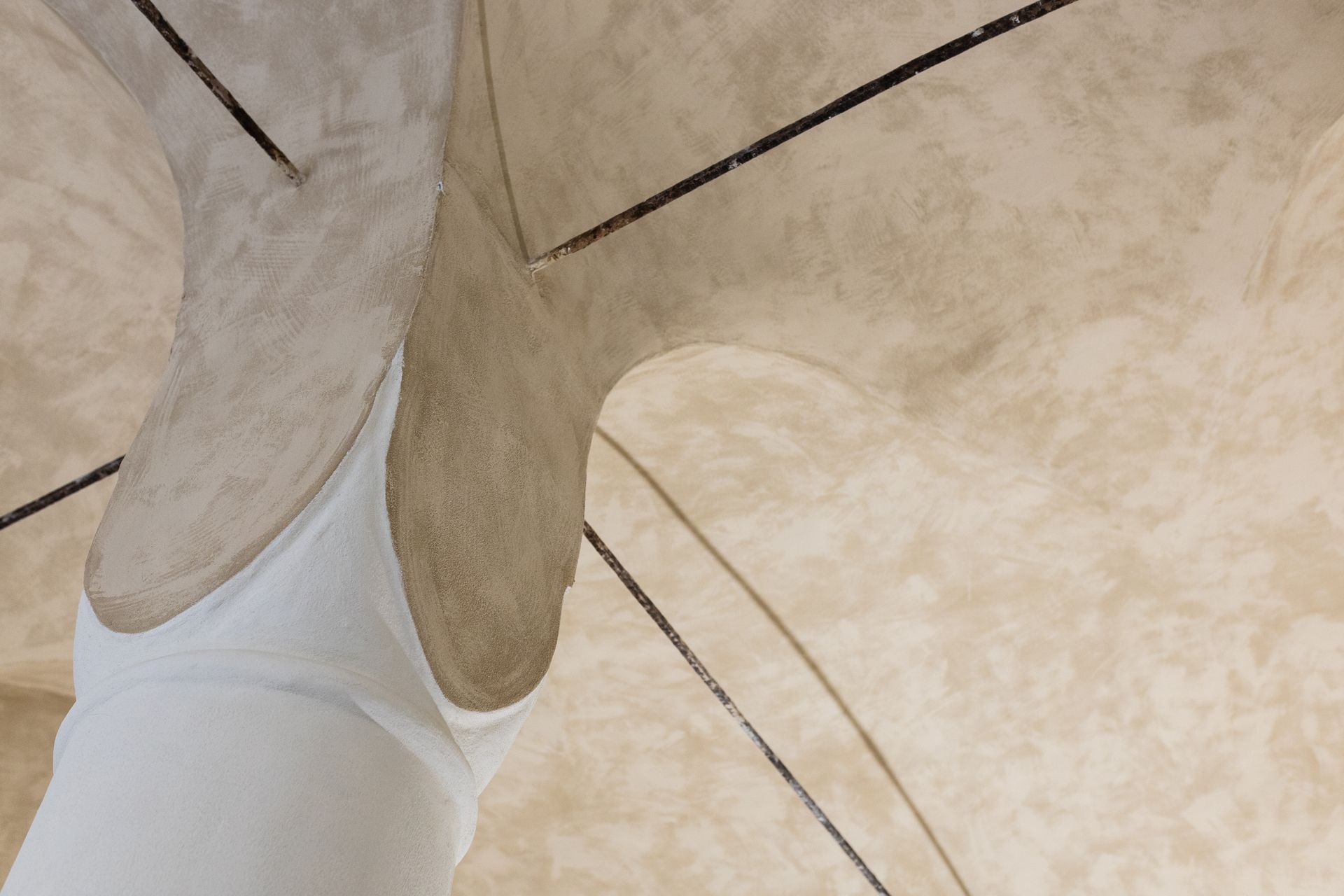 Primo piano di una persona vestita di bianco in piedi su una superficie architettonica curva di colore beige.