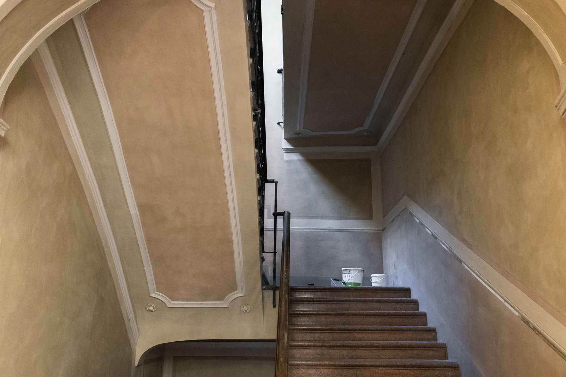 Vano scale con gradini in legno, pareti beige e ringhiera bianca, visto dall'alto.