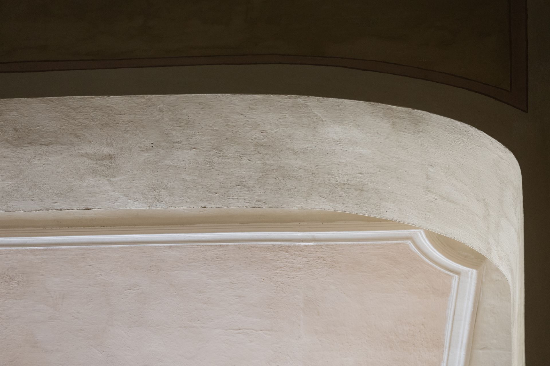 Primo piano dello schienale di una sedia imbottita beige con bordino bianco e dettaglio angolare curvo.
