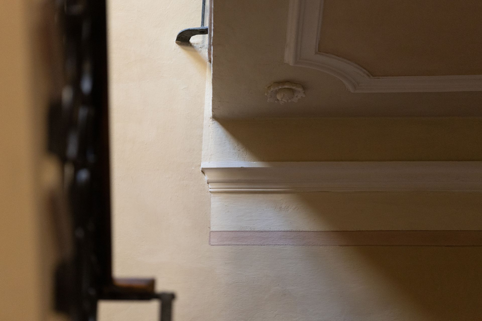 Primo piano di una parete beige con modanature decorative e, sulla sinistra, di un telaio di porta scuro parzialmente visibile.