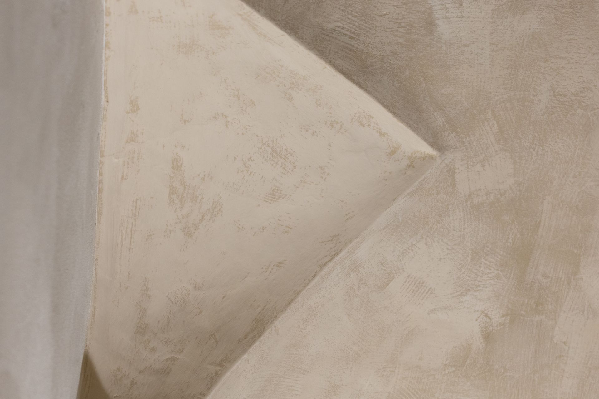 Parete astratta beige con texture e una netta piega geometrica triangolare al centro.