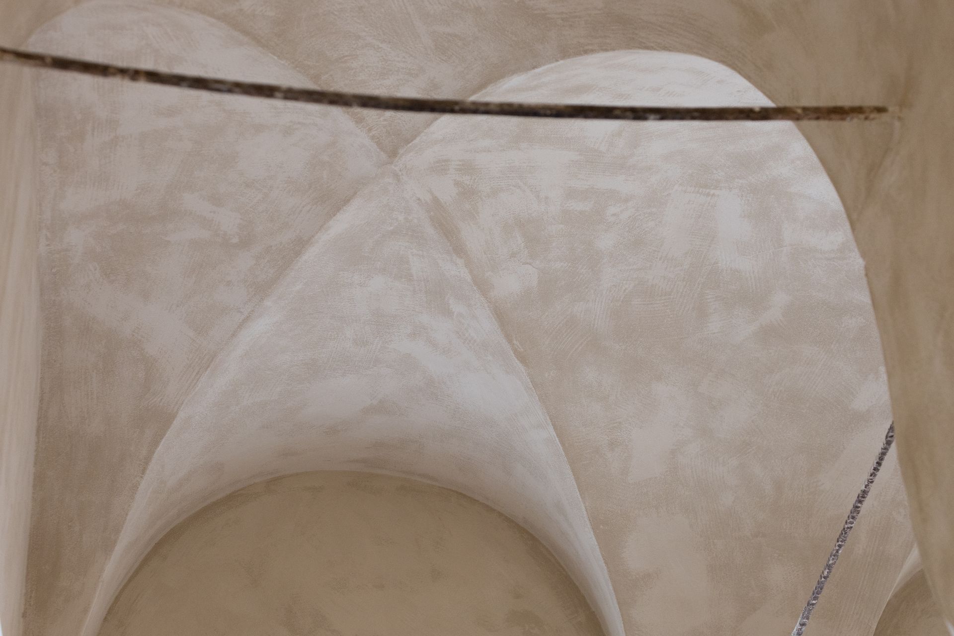Primo piano di un soffitto a volta in gesso beige con curve ad arco e texture usurata.