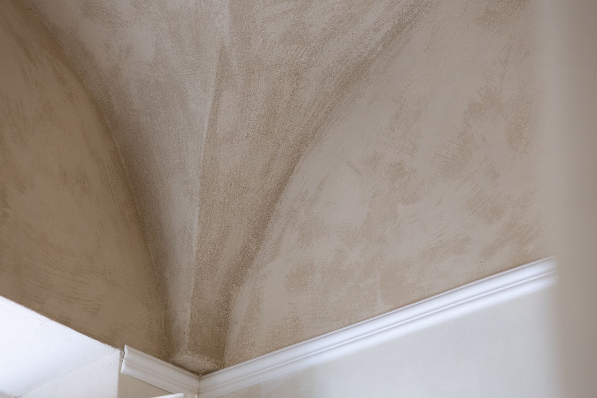 Angolo di una stanza con pareti beige dalla texture particolare che incontrano cornici e modanature bianche.