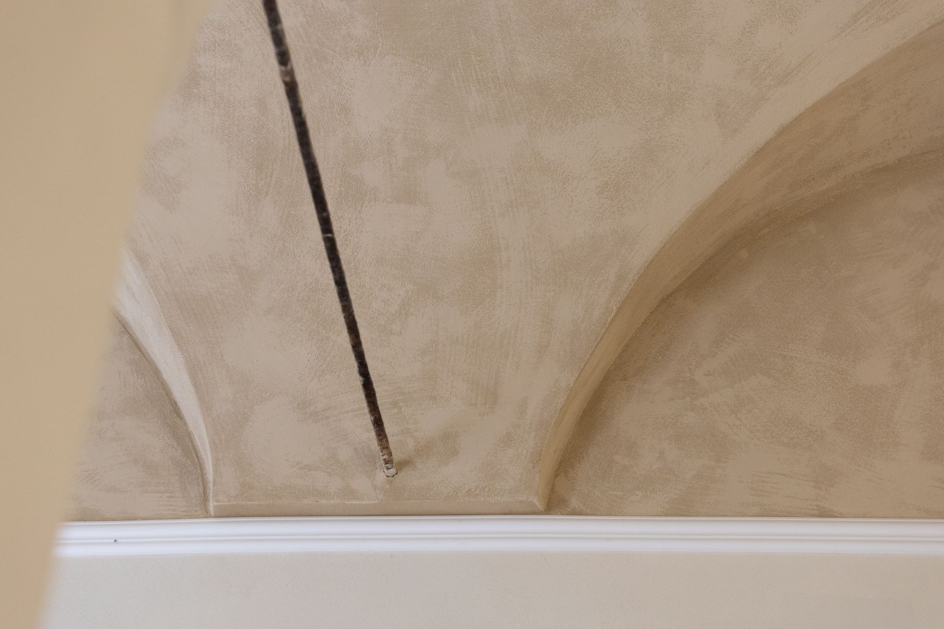 Soffitto a volta beige con un cordone scuro sospeso sopra una cornice o mensola bianca