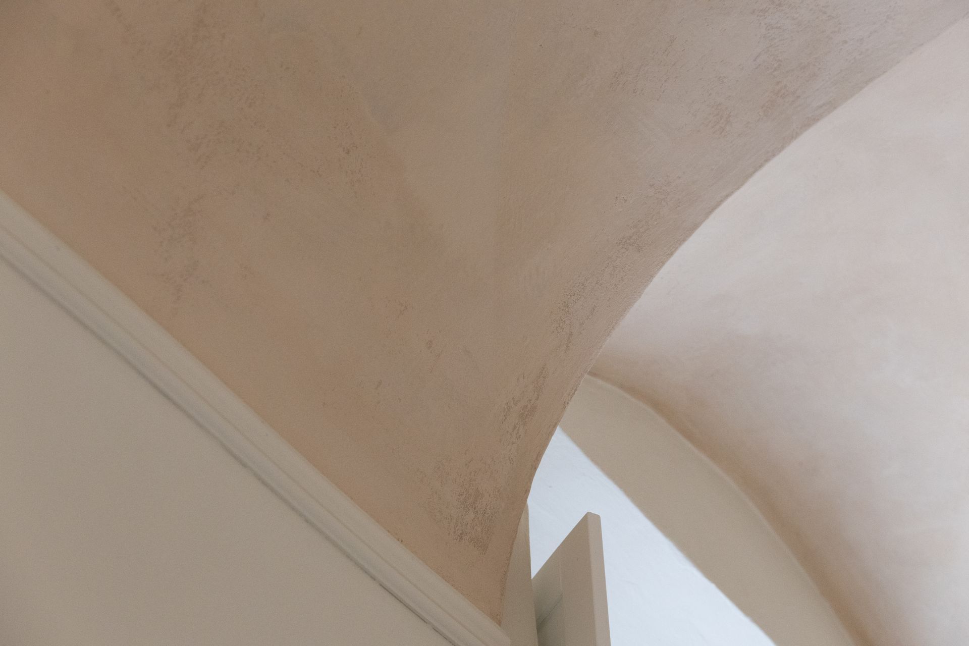 Arco curvo in stucco beige e bianco contro un cielo pallido