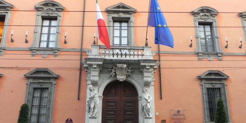 Bandiere francesi e dell'UE sopra l'ingresso decorato di un edificio arancione con portale ad arco.