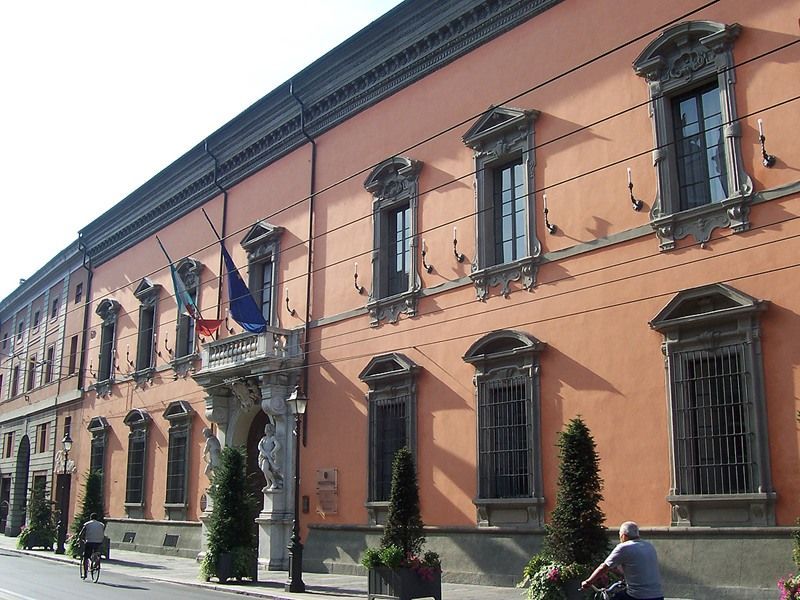 Edificio governativo storico color pesca con finestre ad arco, bandiere e persone che passeggiano all'esterno.