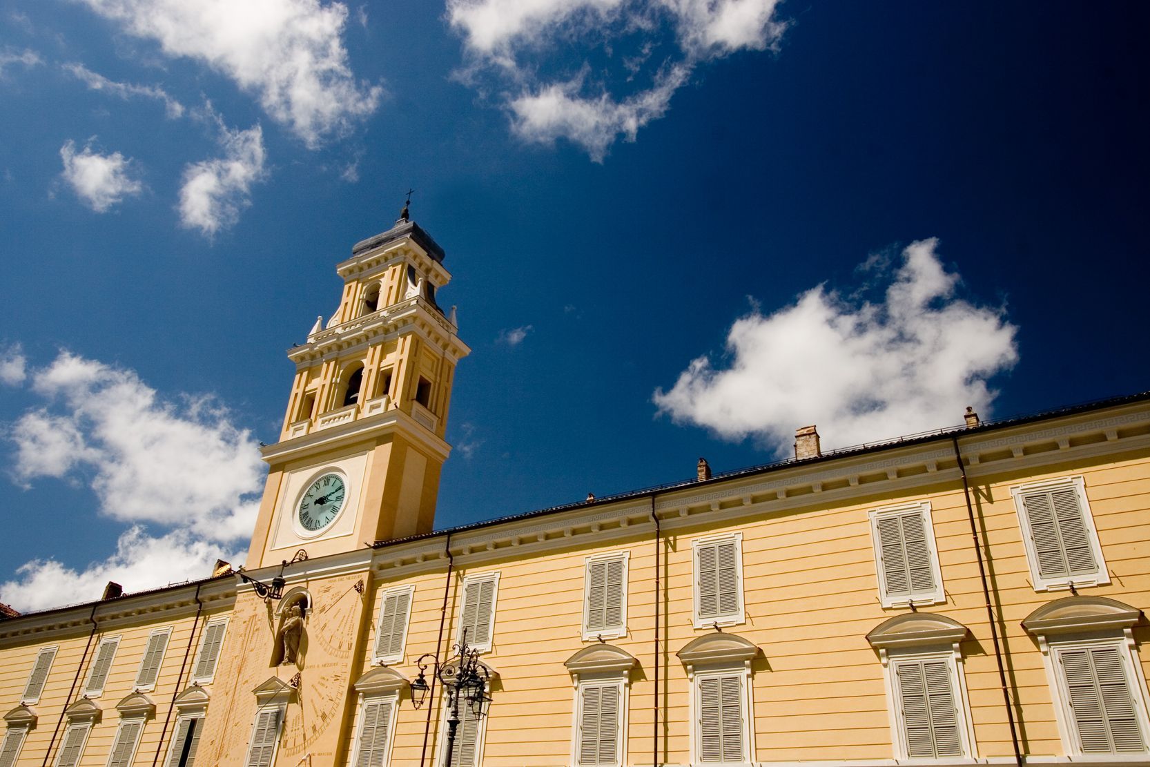 Edificio storico color beige con torre dell'orologio sullo sfondo di un cielo blu con nuvole.
