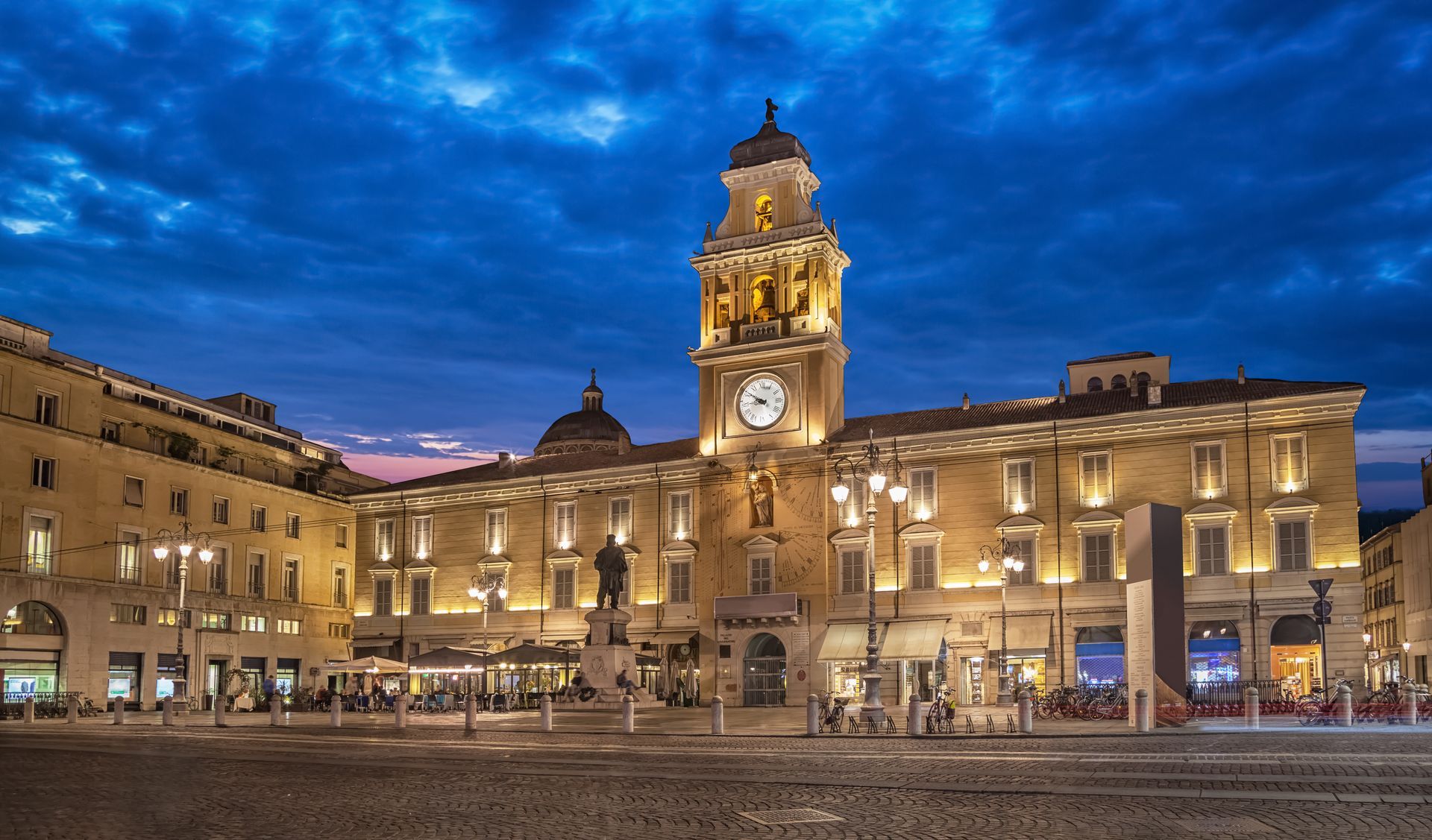 Il municipio storico illuminato al crepuscolo in una piazza lastricata con torre dell'orologio e cielo azzurro.