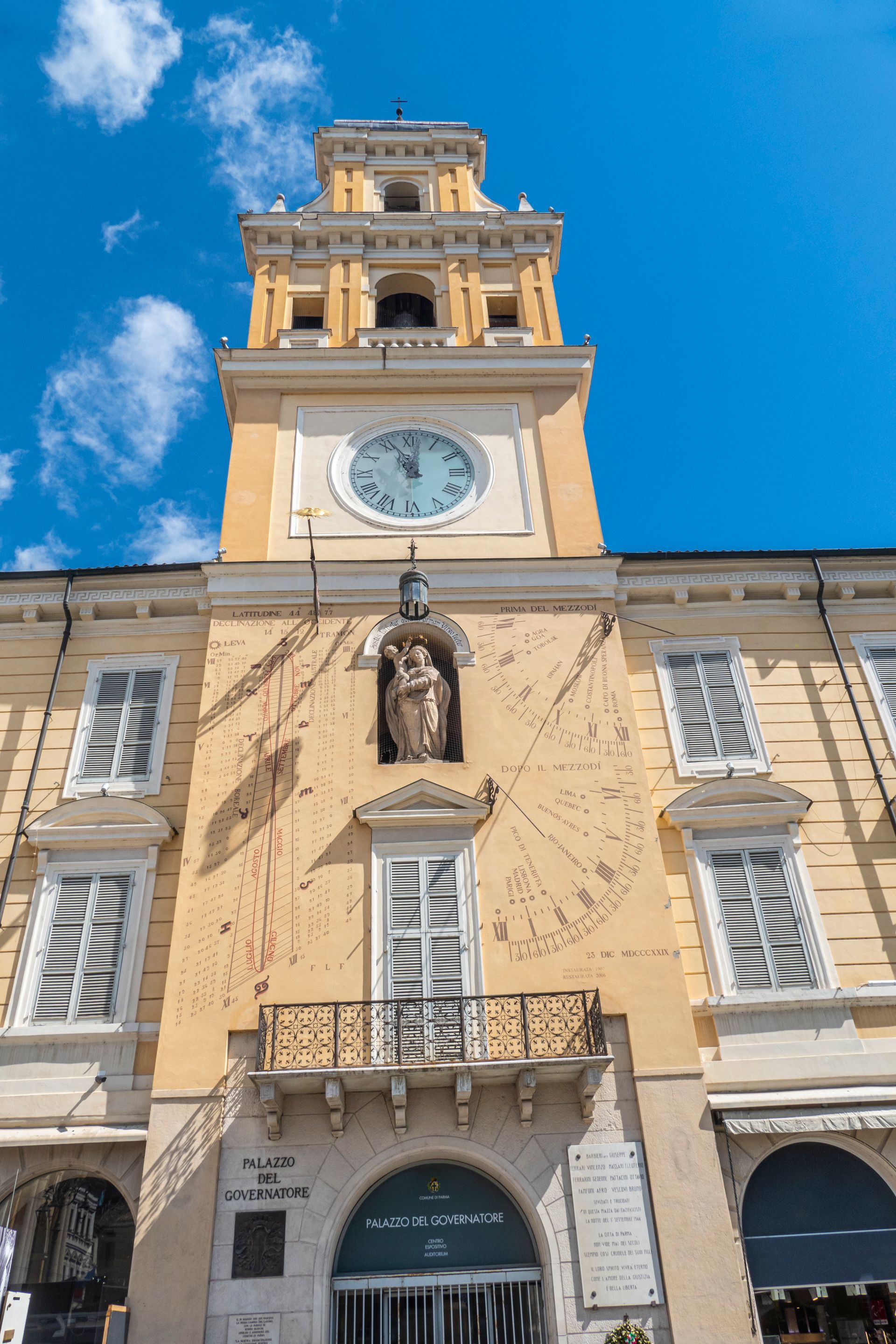 Facciata storica della torre dell'orologio con statua, pareti color crema e cielo blu.