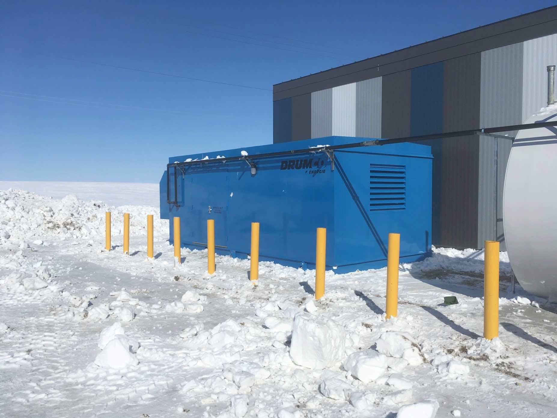 Un conteneur bleu est posé dans la neige à côté d'un bâtiment.