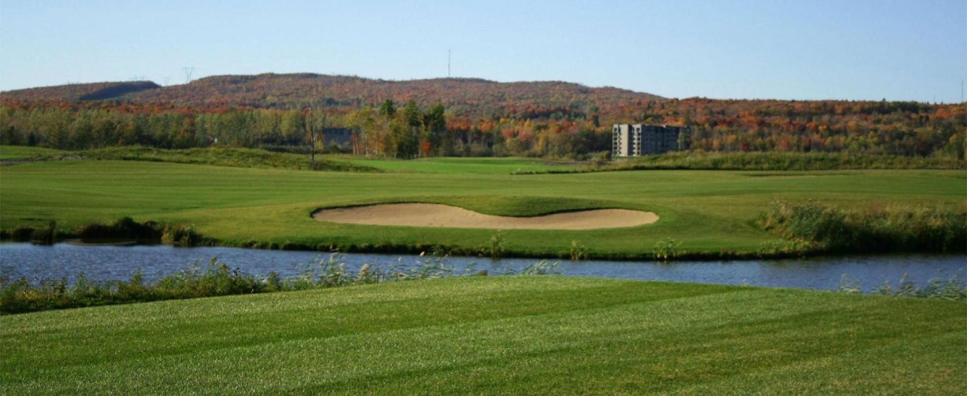 Un parcours de golf avec un étang et des montagnes en arrière-plan.
