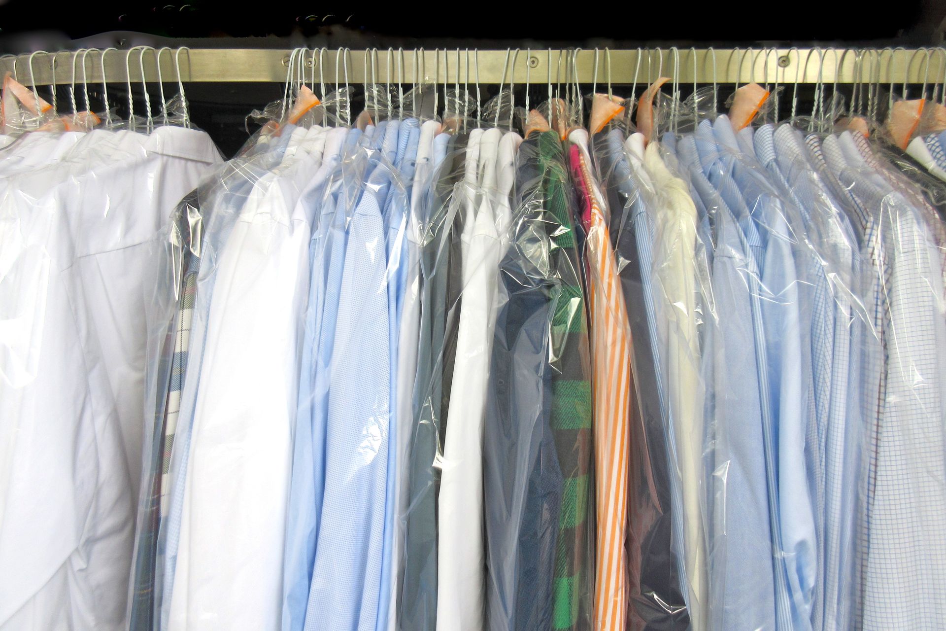A row of blue shirts hanging on a rack in a dry cleaner.
