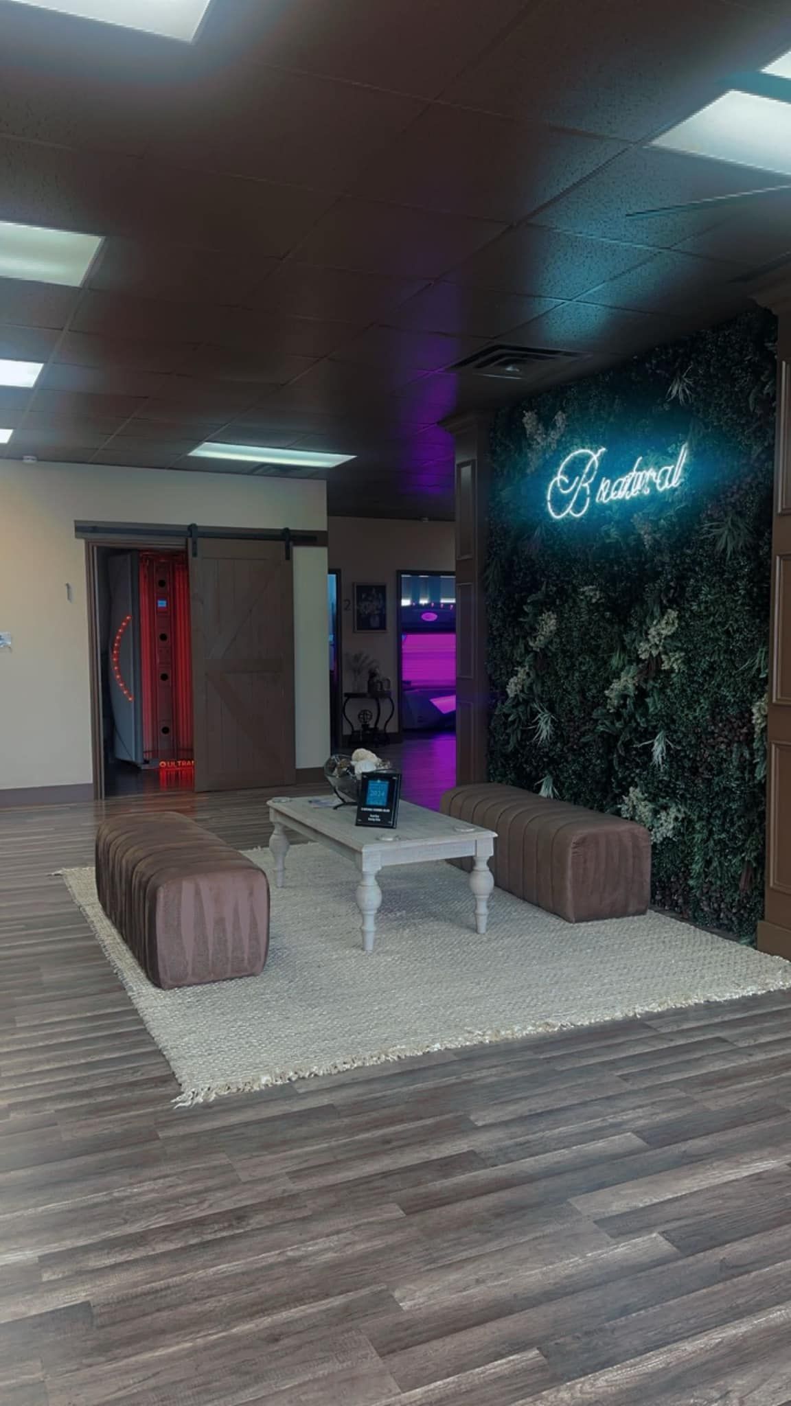A room with a table and benches in it and a neon sign on the wall.