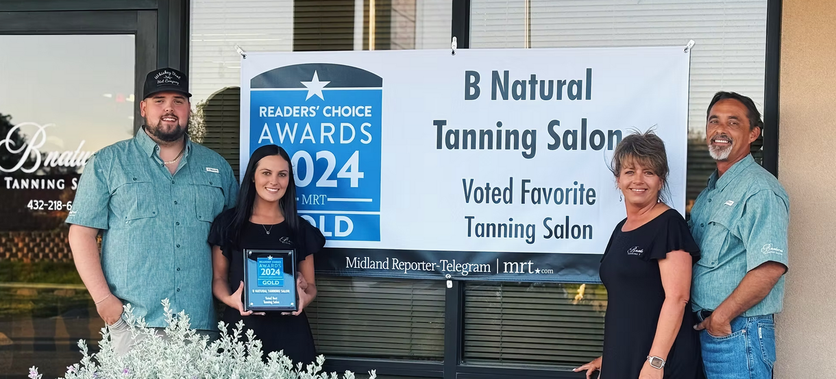 A group of people standing in front of a b natural tanning salon sign.