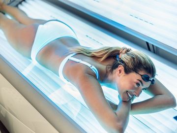 A woman in a bikini is laying in a tanning bed.