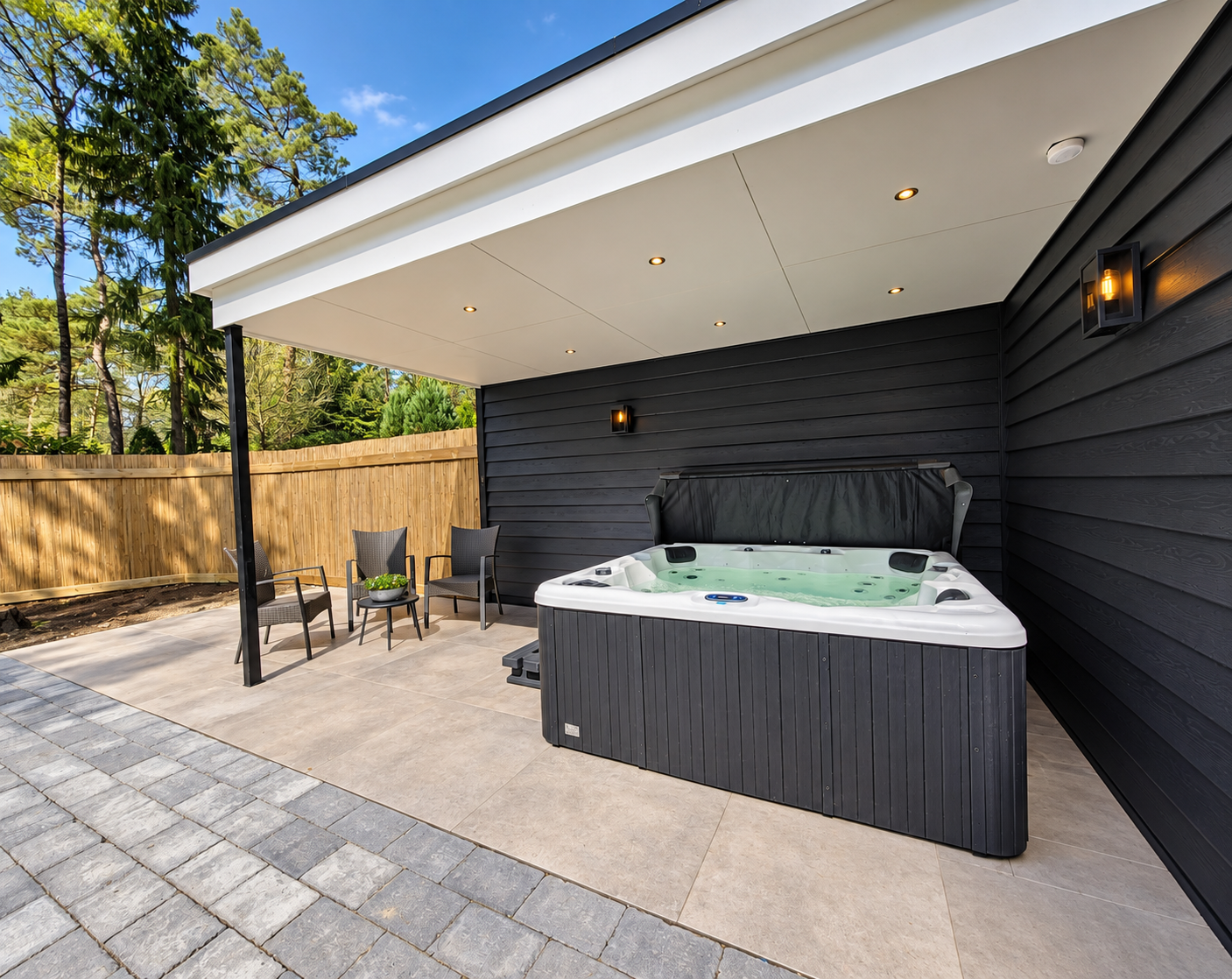 Buitenpatio met een overdekte jacuzzi, grijze gevelbekleding en een kleine tafel met stoelen bij een houten schutting.