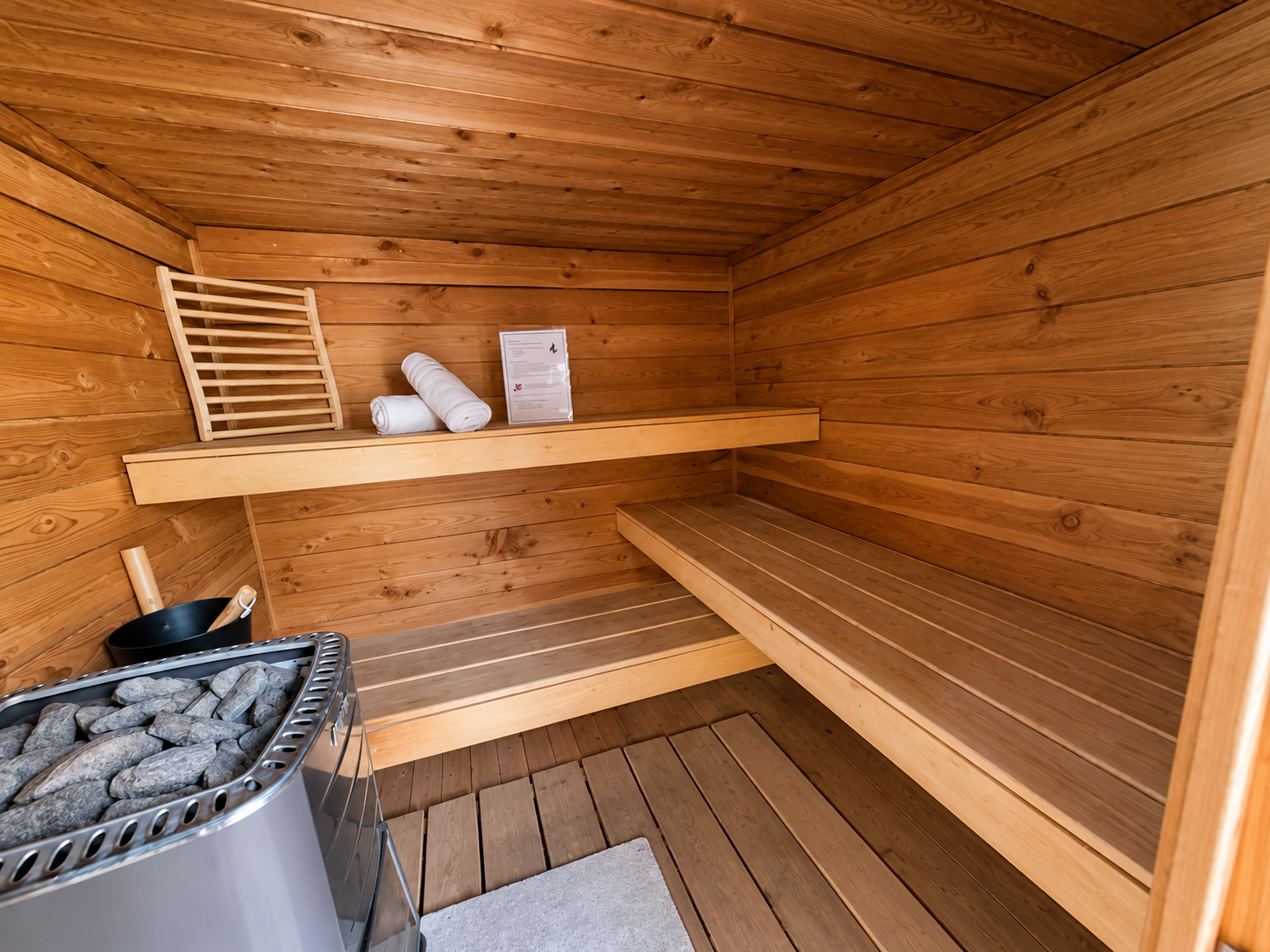 Sauna met houten lambrisering, zitbanken, verwarmingsstenen en een emmer en lepel binnenin.