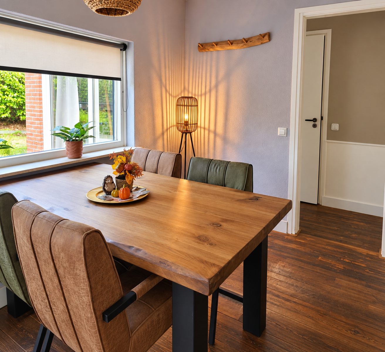 Moderne eetkamer met houten tafel, gestoffeerde stoelen, vensterbank en sfeervolle lampverlichting.