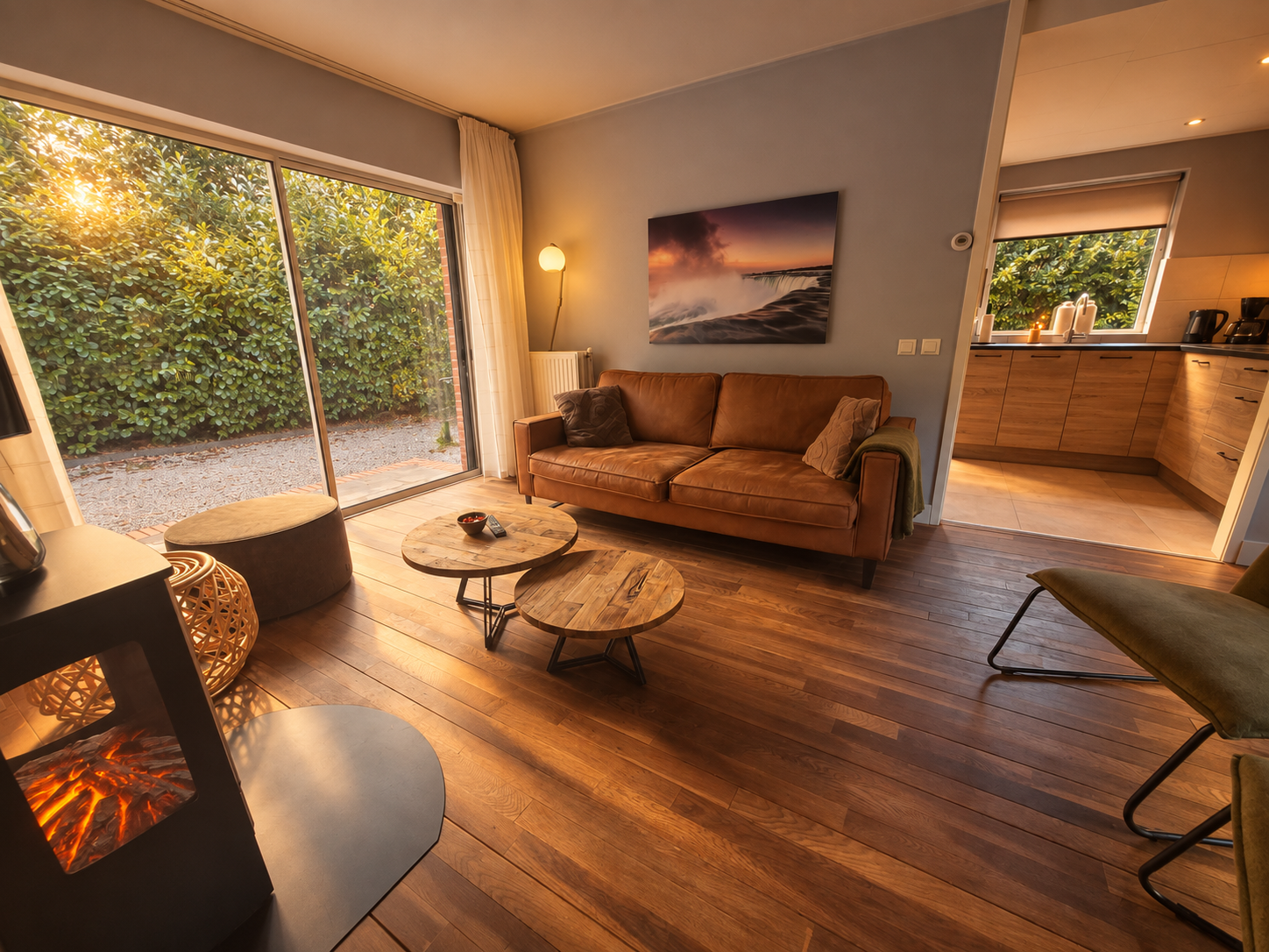 Gezellige woonkamer met houten vloer, bank, ronde tafels en zonsonderganglicht door grote ramen.