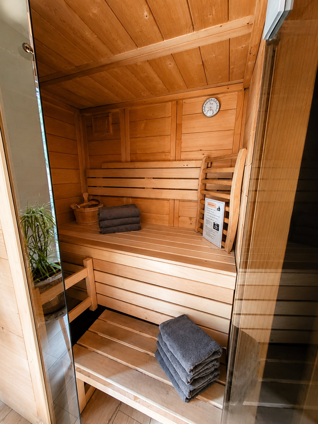 Sauna met houten lambrisering, twee houten banken, opgevouwen grijze handdoeken en een thermometer.