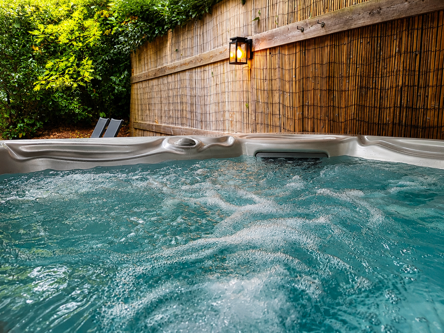 Een jacuzzi in de achtertuin met borrelend blauw water, omgeven door een bamboehek en groen uit de tuin.
