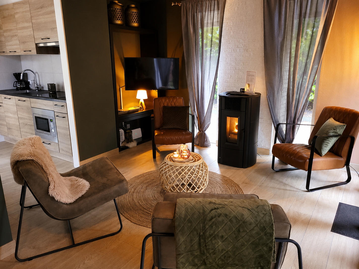 Gezellige woonkamer met fauteuils, een brandende haard, tv, zachte gordijnen en warme verlichting.