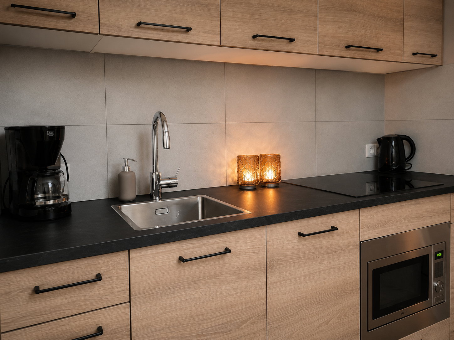 Moderne keuken met aanrechtblad, spoelbak, zwarte apparaten, houten kastjes en brandende kaarsen op de achterwand.