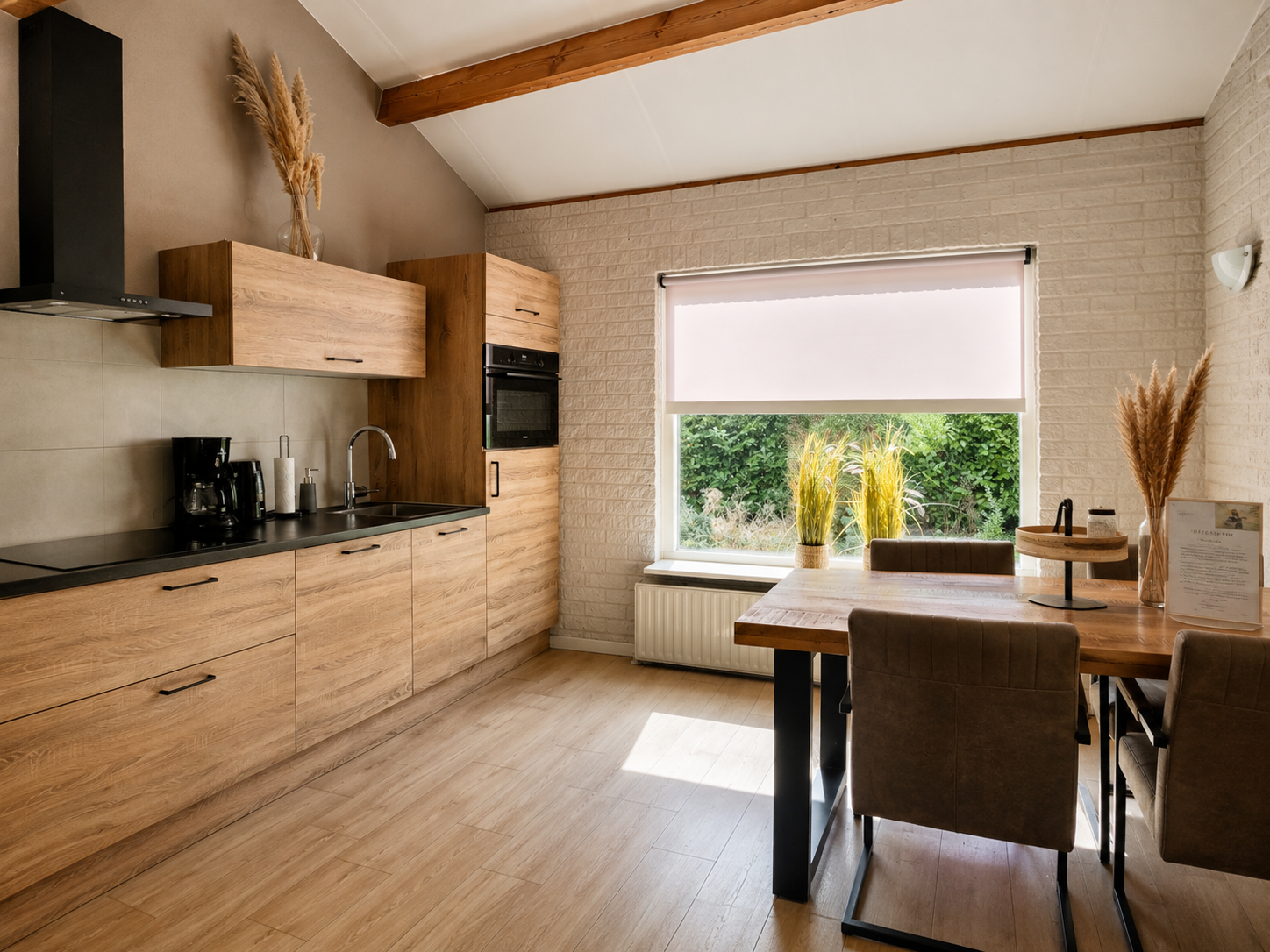 Moderne keuken en eetruimte met houten kasten, groot raam en eettafel omgeven door groen.